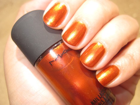 Een hand met een oranjerode duochrome shimmer nagellak met een nagellak van dezelfde kleur