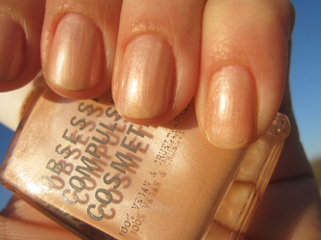 Een hand met een lichte crème abrikozenbeige met een semi-ondoorzichtige zilverachtige shimmer finish nagellak met een nagellak van dezelfde kleur
