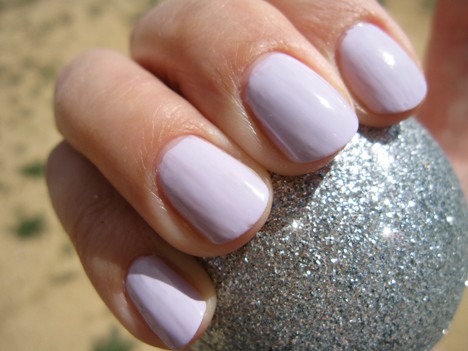 Een hand met een lichtpaarse nagellak die een zilveren met glitterbal vasthoudt
