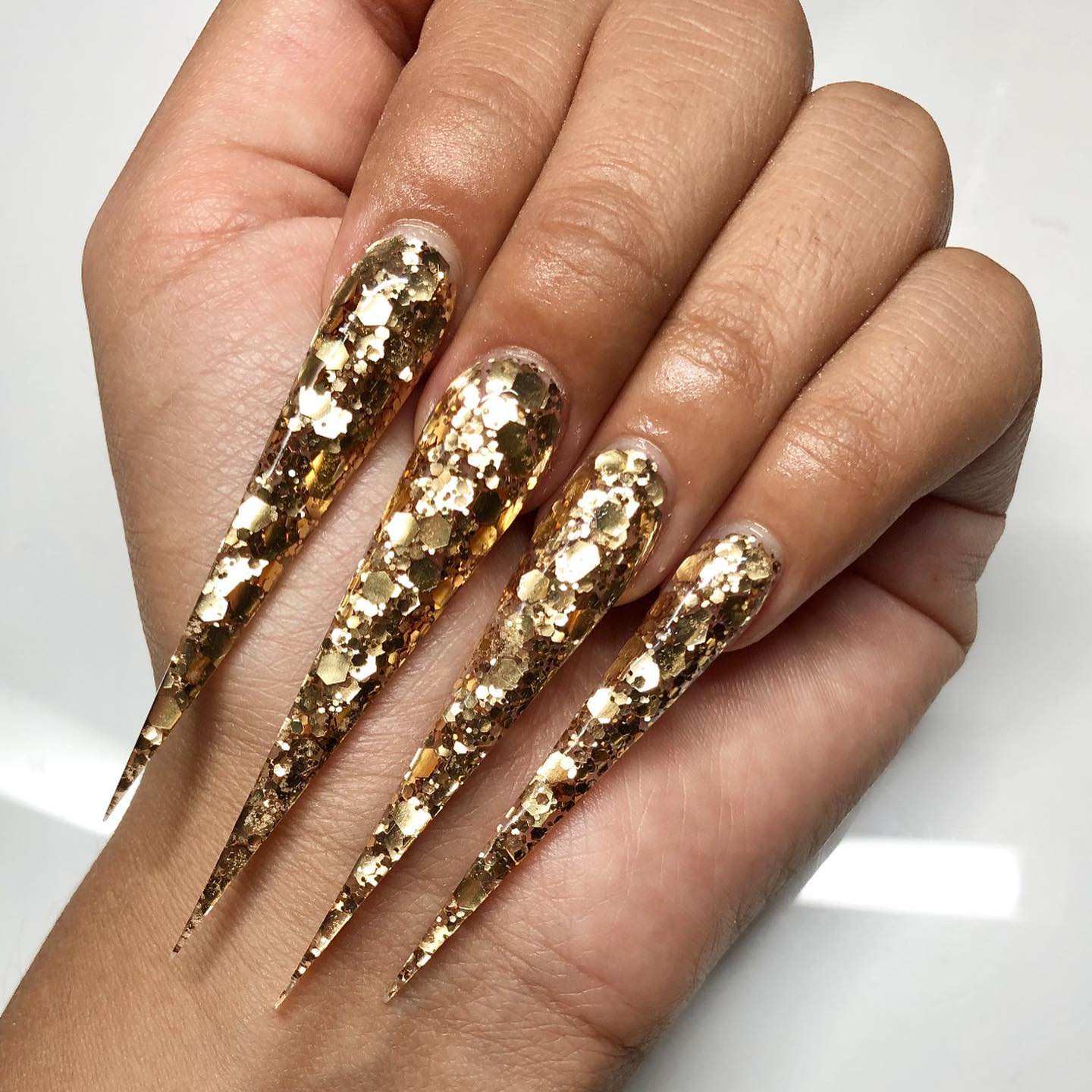 Zeer lange stiletto nagels met gouden glitter