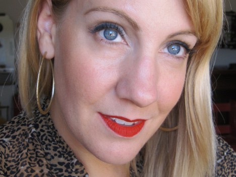 Een blondharige vrouw met een rode lippenstift, die glimlachend naar de camera kijkt 