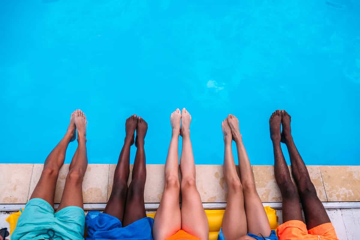Vijf mensen in badpakken met hun benen over de rand van een zwembad