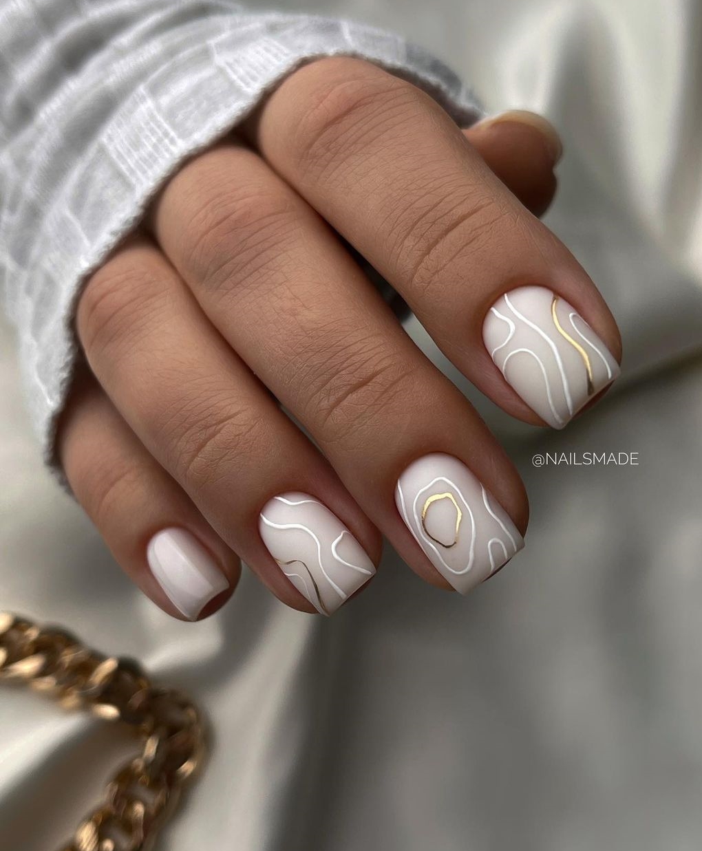 Korte matte witte nagels met witte en gouden wervelingen