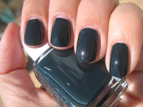Een hand met een zwartgeblakerde groenblauwe nagellak met een essie nagellak