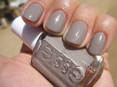 Een hand met een grijze cementnagellak met een essie nagellak