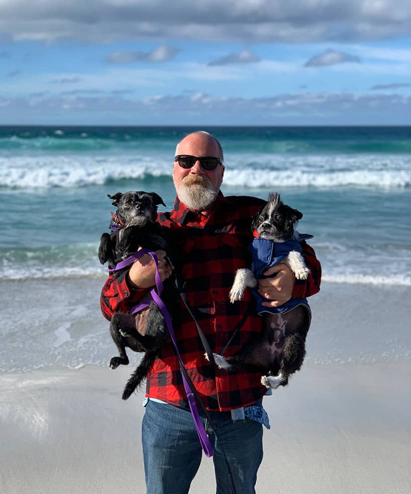 Een man met twee pups die een foto maken op het strand
