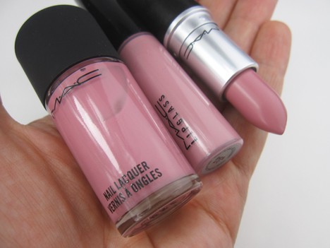 Een hand met MAC lipstick, lipglas en nagellak in een koele roze tint